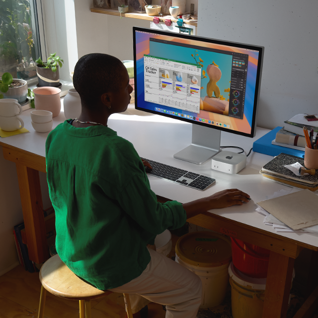 En person ved en pult bruker en Mac mini og en skjerm til å jobbe i apper, som gir fargerike aktiviteter på skjermen